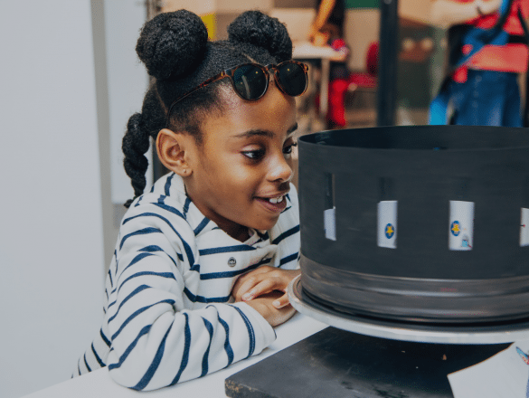 A child watches a zoetrope closely.