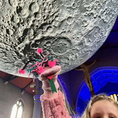 A large moon installation with a young girl holding up a puppet underneath