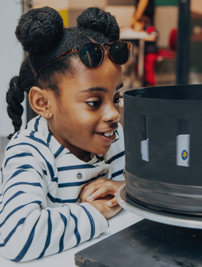 A child watches a zoetrope closely.