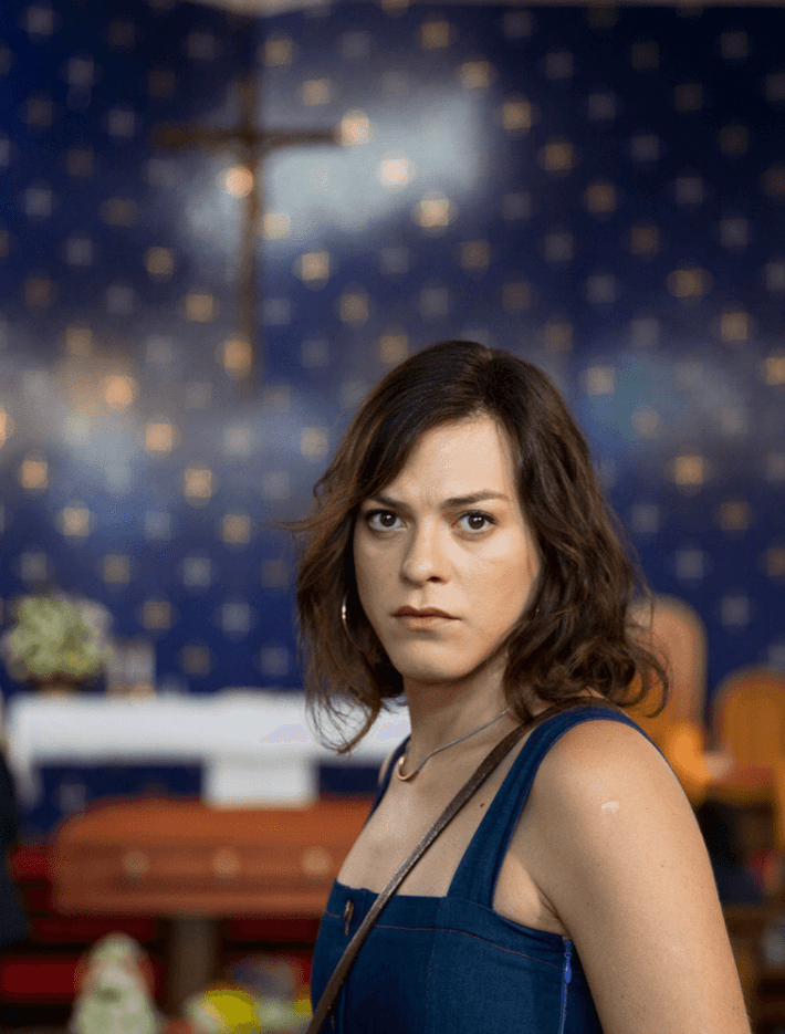 A woman looks into the camera, with a cross behind her.