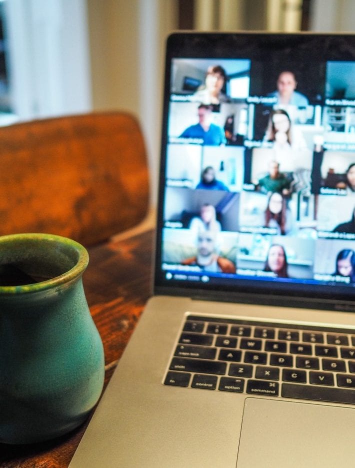 Photo of a table with cup next to a laptop featuring multiple images of people on a webinar
