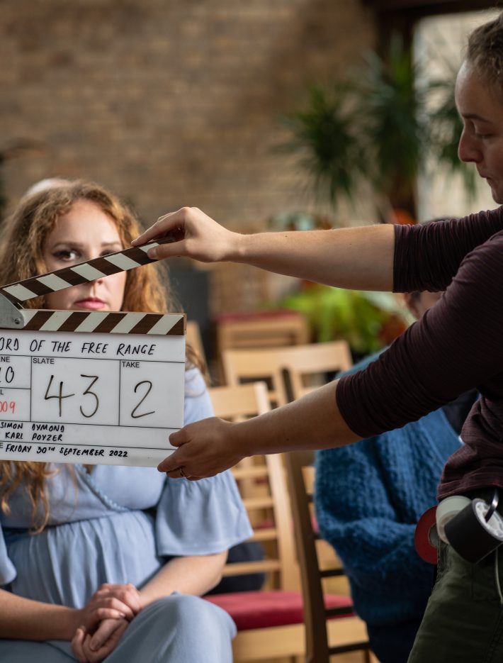 A woman holding a clapperboard in front of an actress on the shoot for Lord of the Free Range