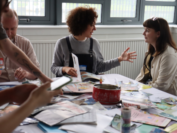 Two women sat at the collage table at Filmcamp 2023 are engaged in a conversation whilst crafting