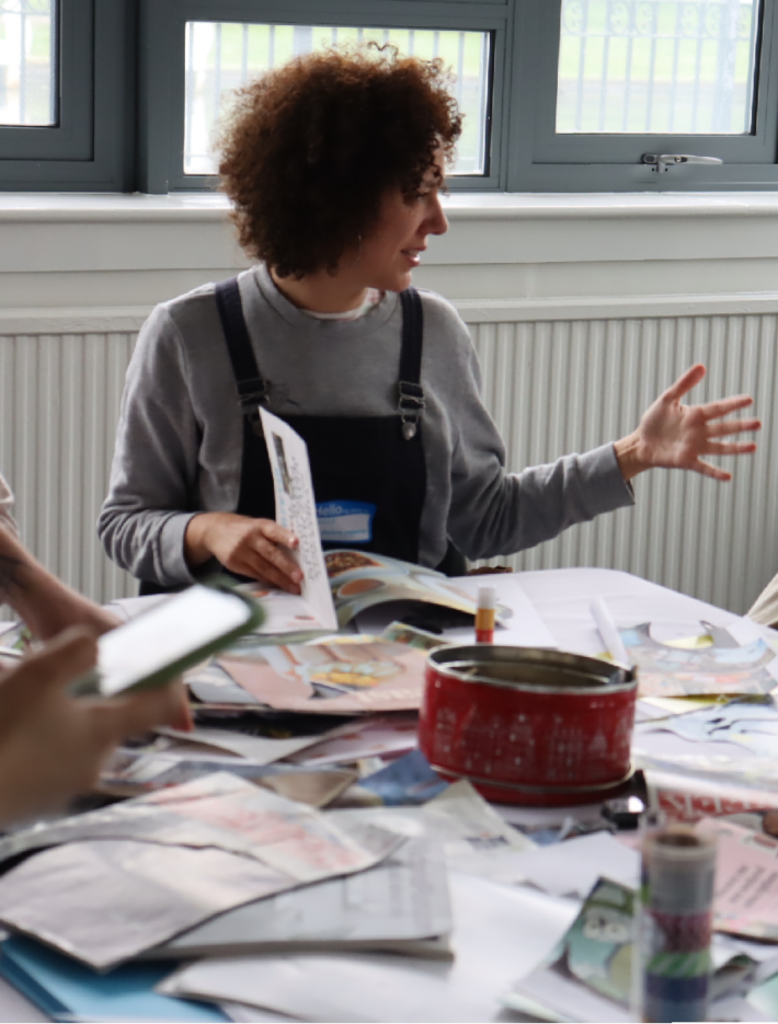 Two women sat at the collage table at Filmcamp 2023 are engaged in a conversation whilst crafting