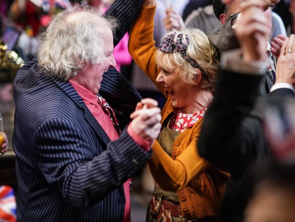Two people amongst a crowd hold hands at chest height in celebration
