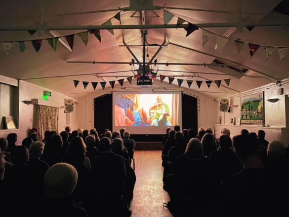 A sold out audience watching a film on a pop up screen.