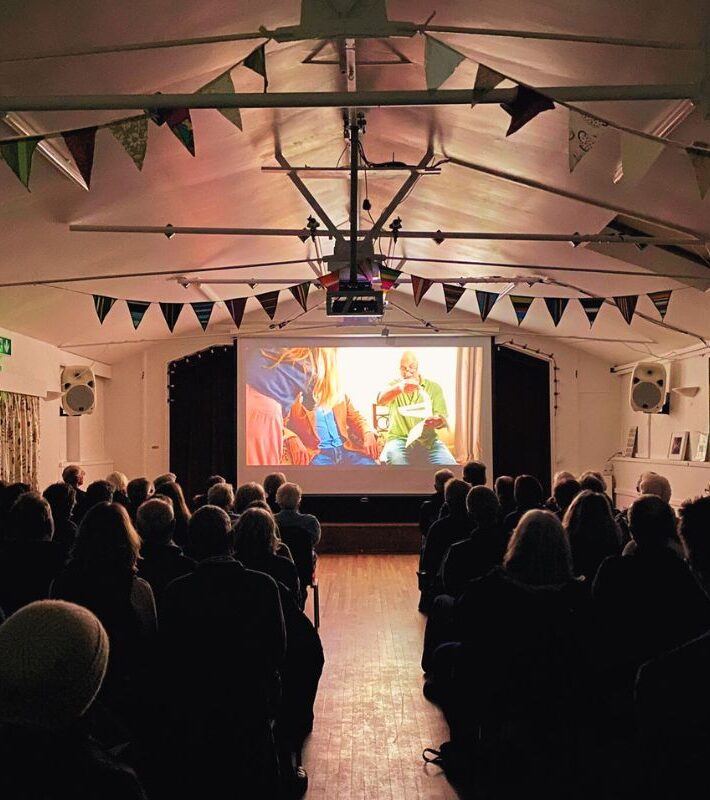 A sold out audience watching a film on a pop up screen.
