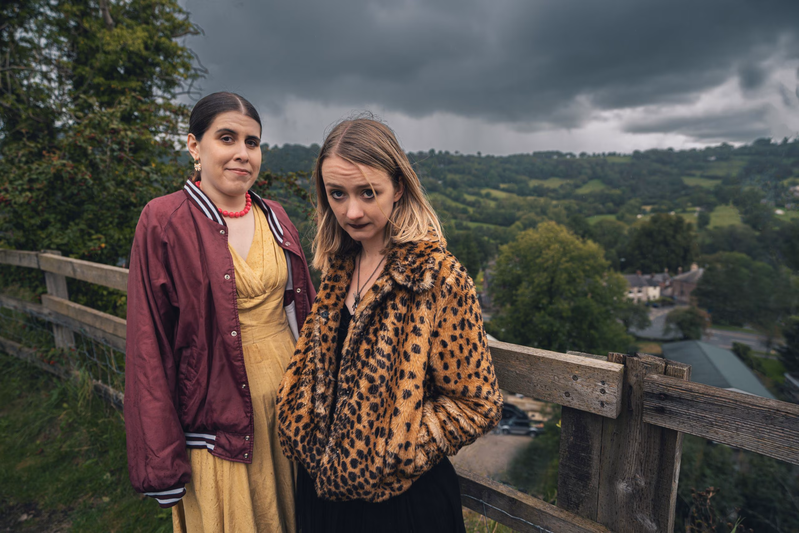 Ada Player and co actor in Peaked look directly at the camera ontop a mountain, Ada wearing a leopard print coat