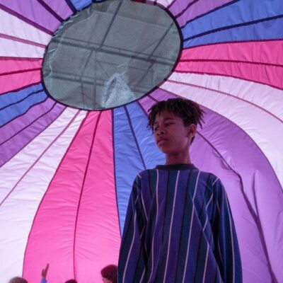 I Saw the TV Glow film still, a young black man stands underneath a multi colour fabric gymnasium dome