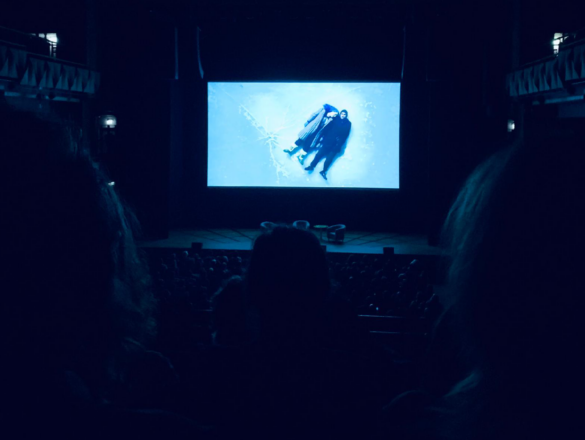 On the screen Eternal Sadness of the Spotless Mind is playing in the cinema lighting the room in blue