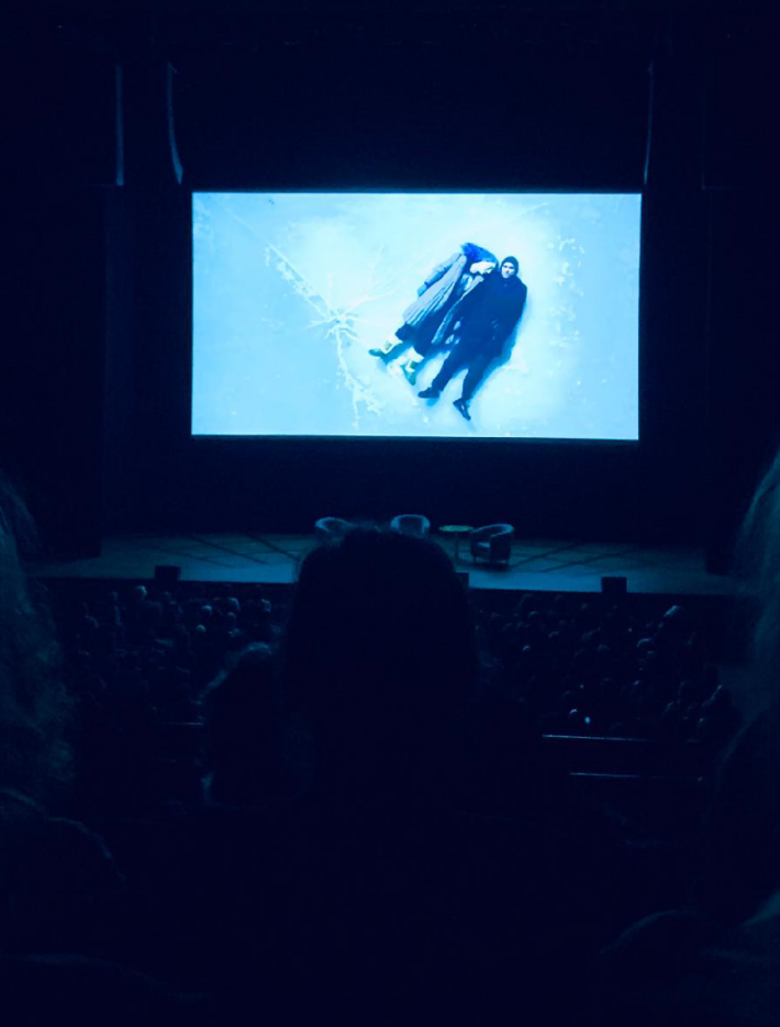 On the screen Eternal Sadness of the Spotless Mind is playing in the cinema lighting the room in blue