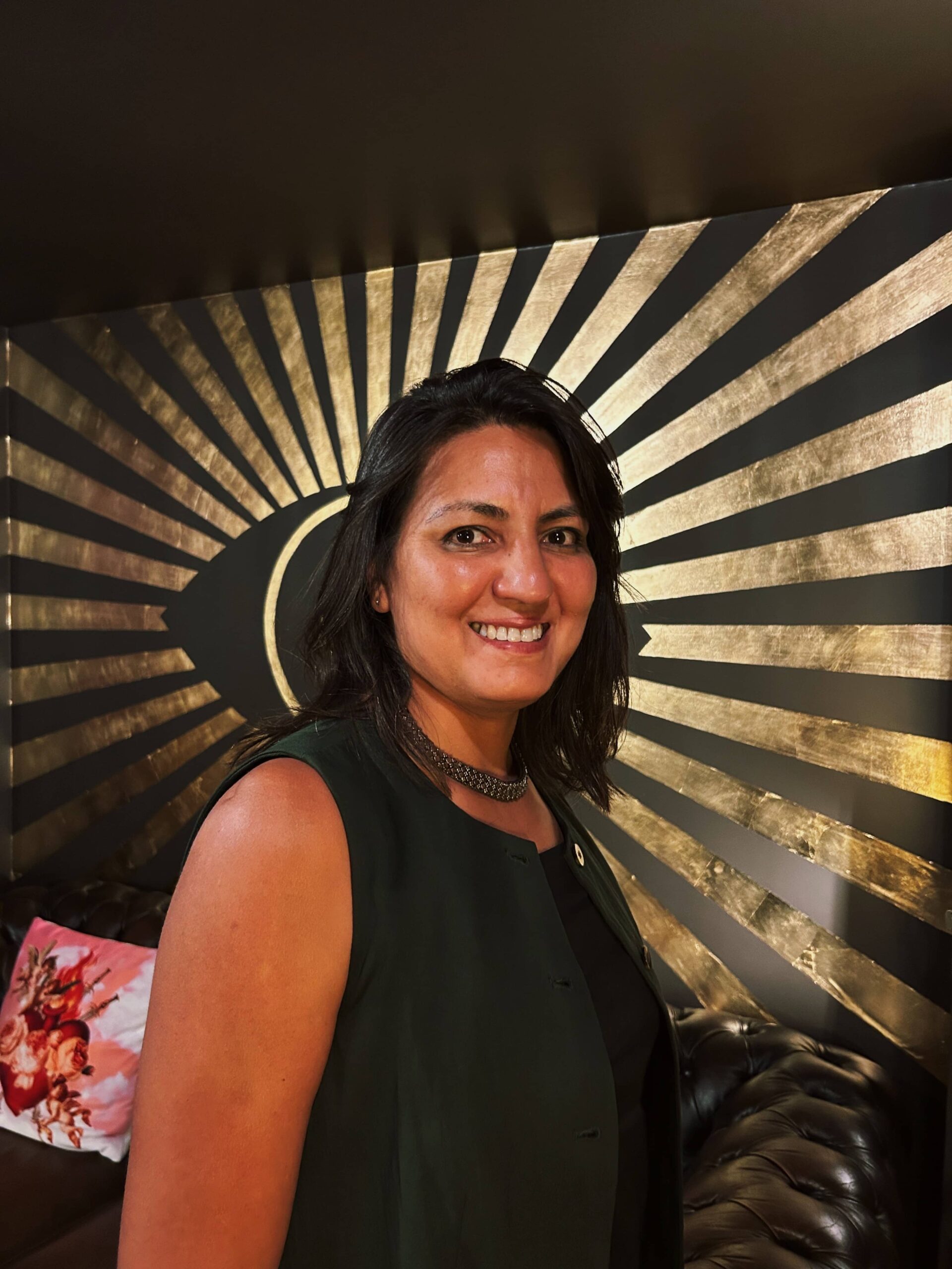 Arij stands smiling in front of the Broadway eye logo painted on a wall in Broadways lounge